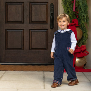 Front view of Louis Longall in midnight blue corduroy worn by a young boy in front of a doorway with greenery and red bows