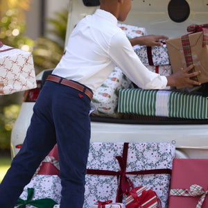 Boy in navy trousers loading wrapped gifts into an open vehicle trunk