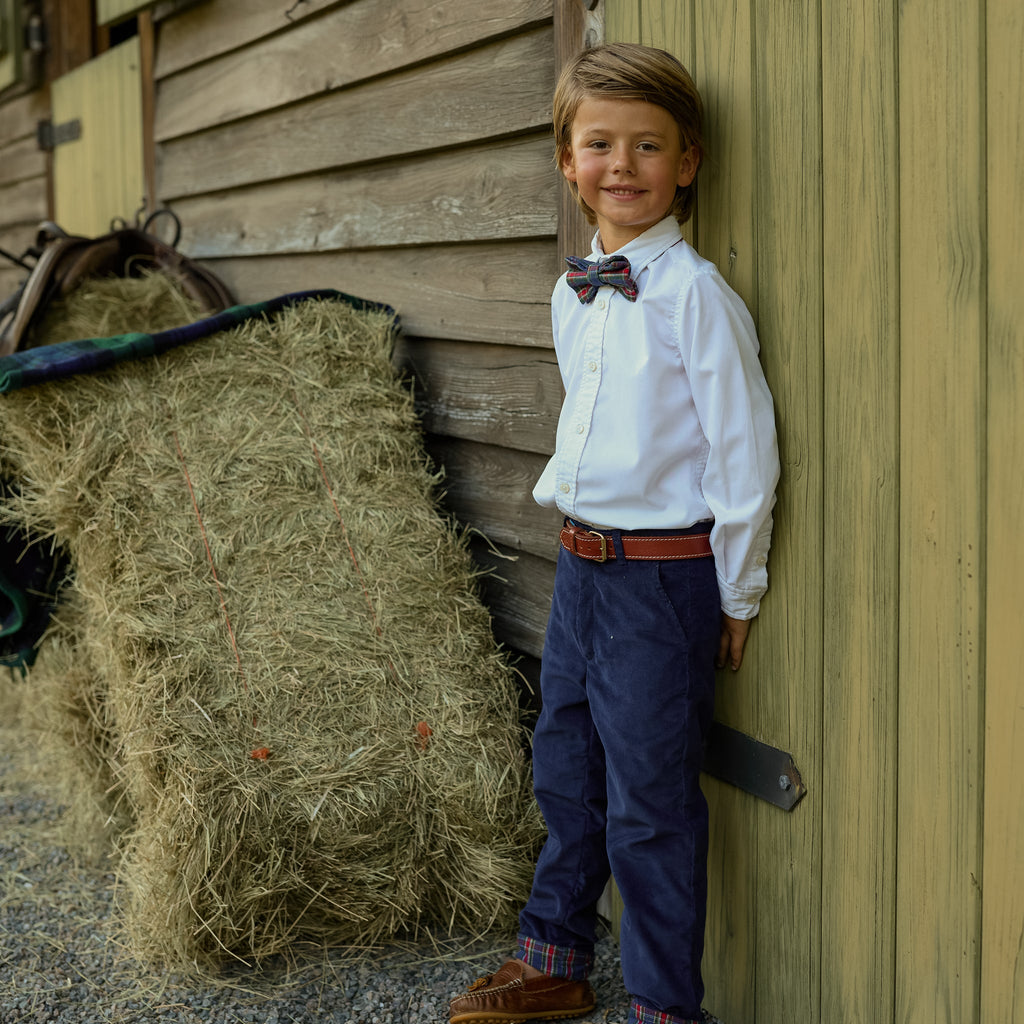 Full-length view of boys’ Bradford Trousers in midnight blue corduroy on a boy beside a hay bale