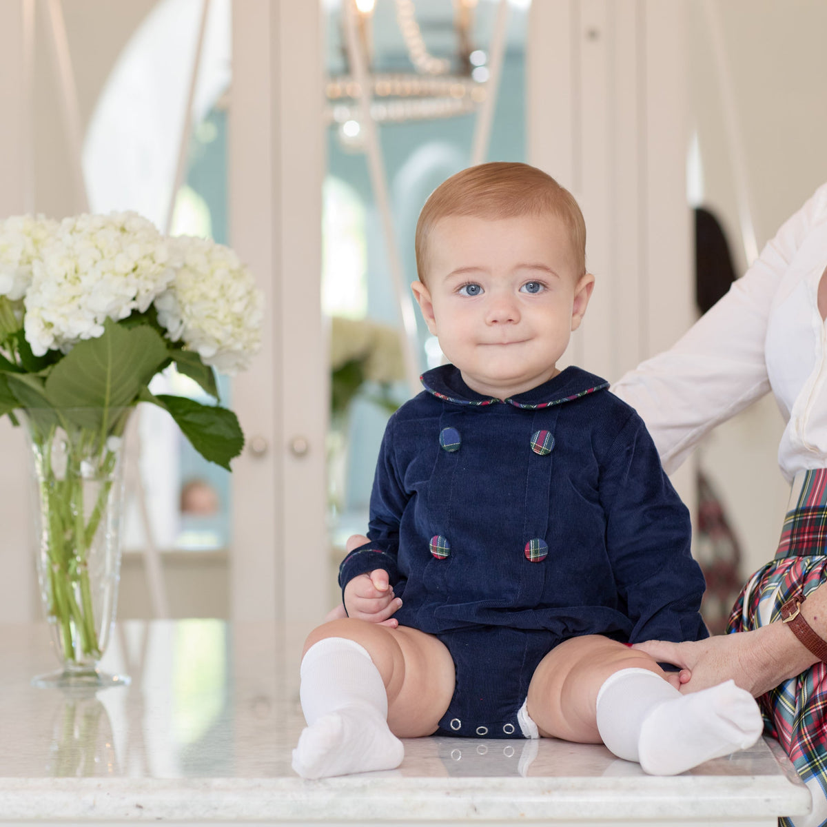 Baby boys’ Banks Bubble in Midnight Blue Corduroy with Tinsel Tartan-covered buttons and coordinating plaid trim at the Peter Pan collar and cuffs.