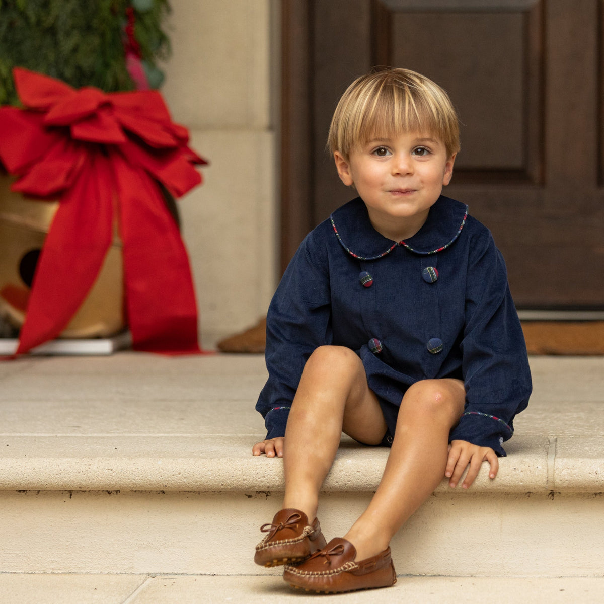 Baby boys’ Banks Bubble in Midnight Blue Corduroy with Tinsel Tartan-covered buttons and coordinating plaid trim at the Peter Pan collar and cuffs.