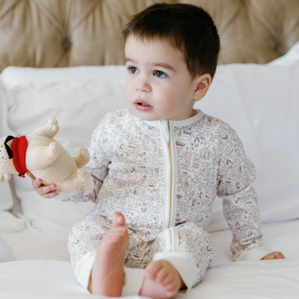 Front view of Good Dog Zip Baby Onesie showcasing ivory fabric, brown dog print, and two-way zipper on white bedding