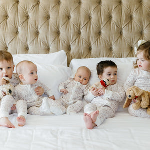 Front view of Good Dog Zip Baby Onesie showcasing brown hand-drawn dog print on babies seated on a bed