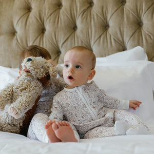 Front view of Good Dog Zip Baby Onesie showcasing ivory fabric with brown hand-drawn dog print on a baby seated on white bedding