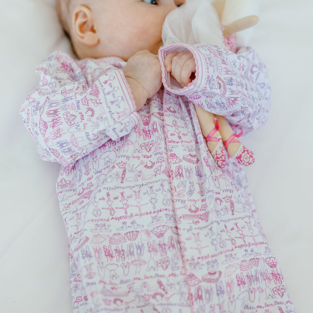 Close-up of Ballet Snap Baby Onesie showcasing pink ballet print and long sleeves on a baby lying on white bedding