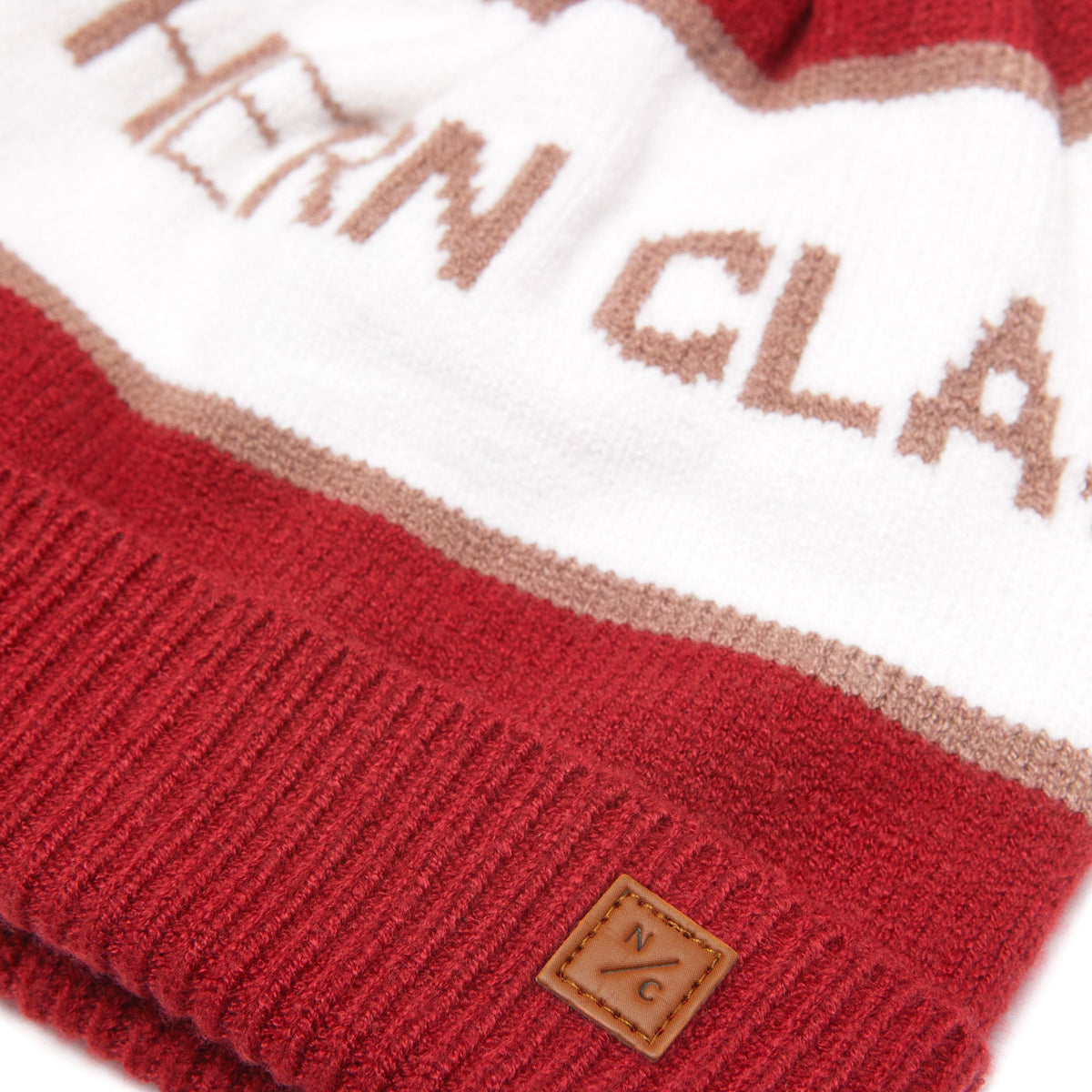 Close-up of knit pom hat showing Heritage Red and Winter White, ribbed cuff, and leather NC logo patch