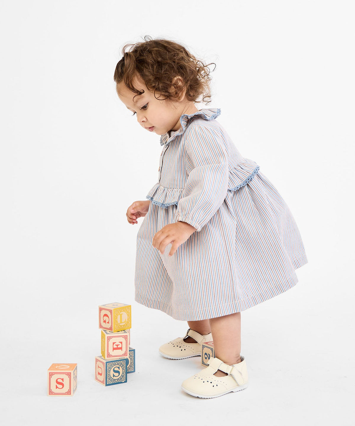 Side view of Hannah baby dress in indigo linen stripe worn by toddler, ruffled lace collar, long sleeves, on white background