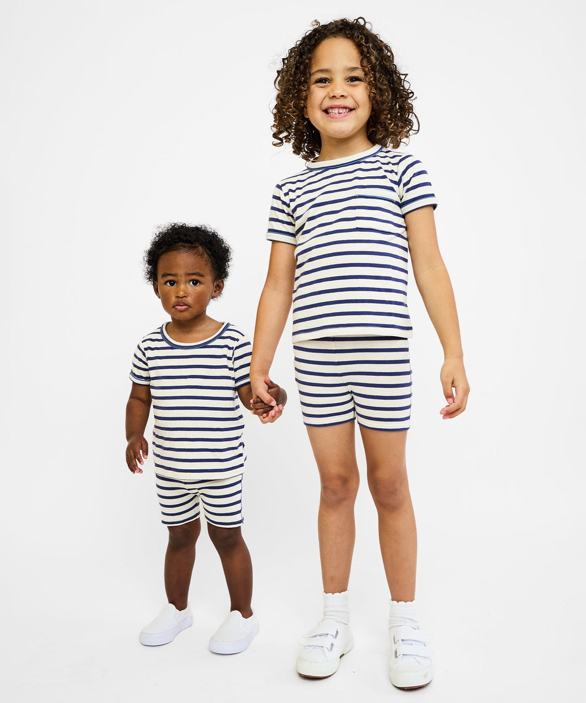 Two children modeling Harley navy and white striped pull-on short sets holding hands on a white background
