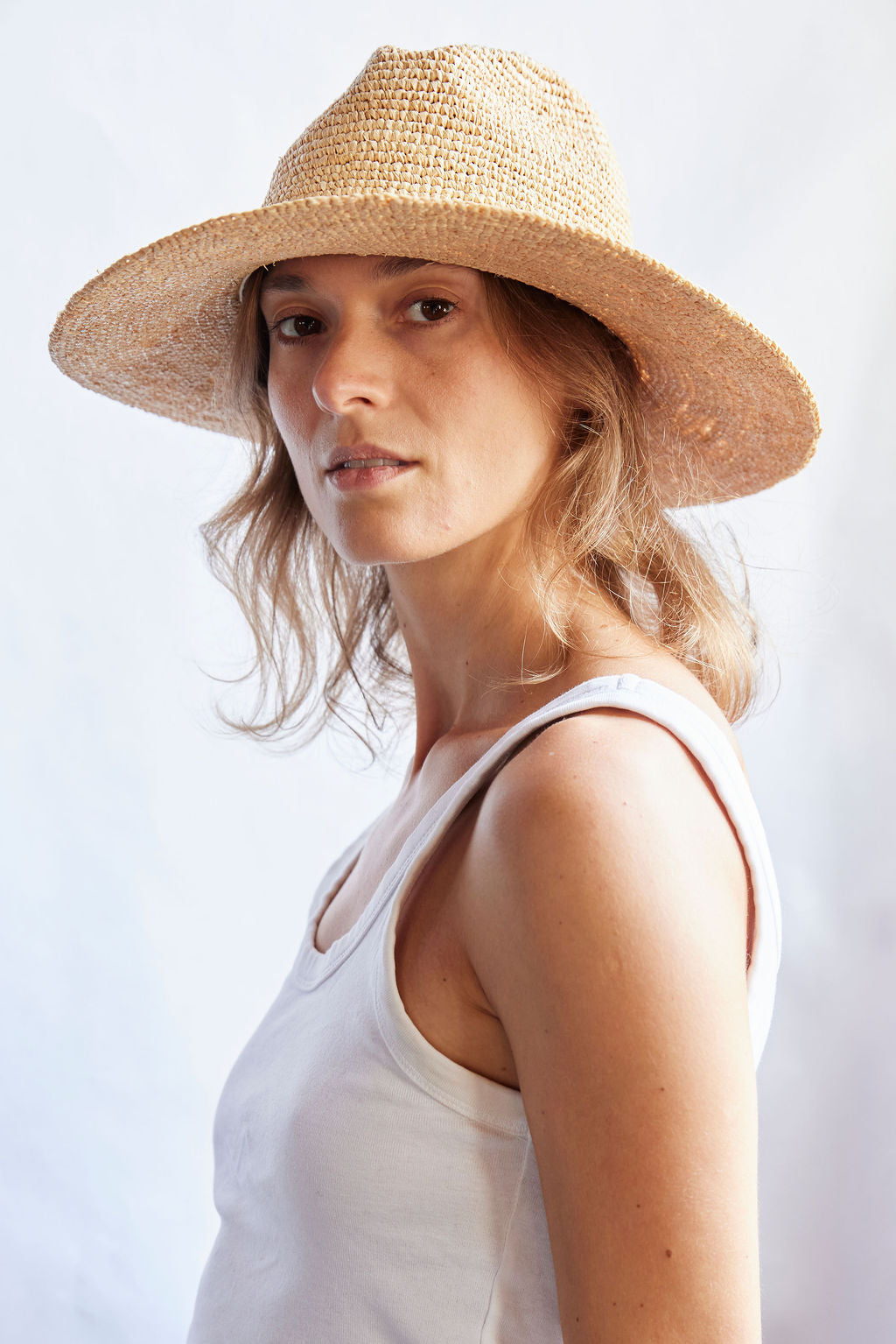 Woman wearing a straw hat and white tank top against a light background