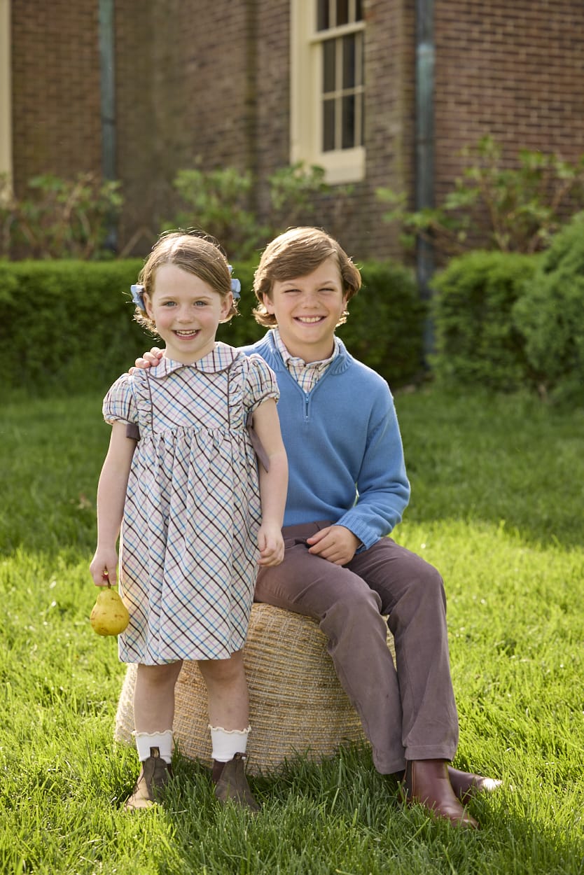 Little English traditional children's clothing. Boys stormy blue quarter zip sweater layered over blue, pink, and brown Wilmington Plaid button down shirt and paired with chocolate brown corduroy classic pants.  Short sleeve peter pan dress in blue, pink, and brown Wilmington Plaid with brown corduroy details for little girls.
