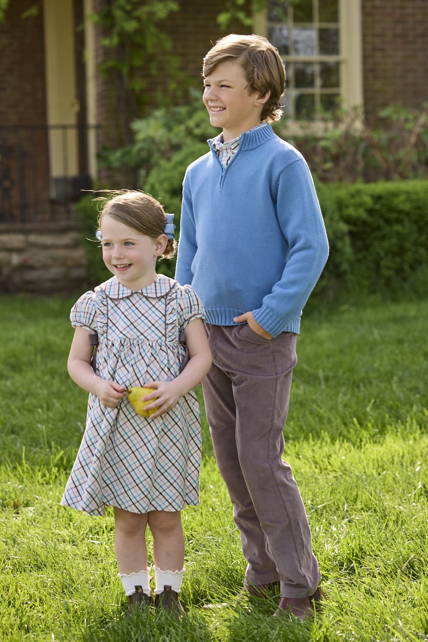 Little English traditional children's clothing. Boys stormy blue quarter zip sweater layered over blue, pink, and brown Wilmington Plaid button down shirt and paired with chocolate brown corduroy classic pants.  Short sleeve peter pan dress in blue, pink, and brown Wilmington Plaid with brown corduroy details for little girls.