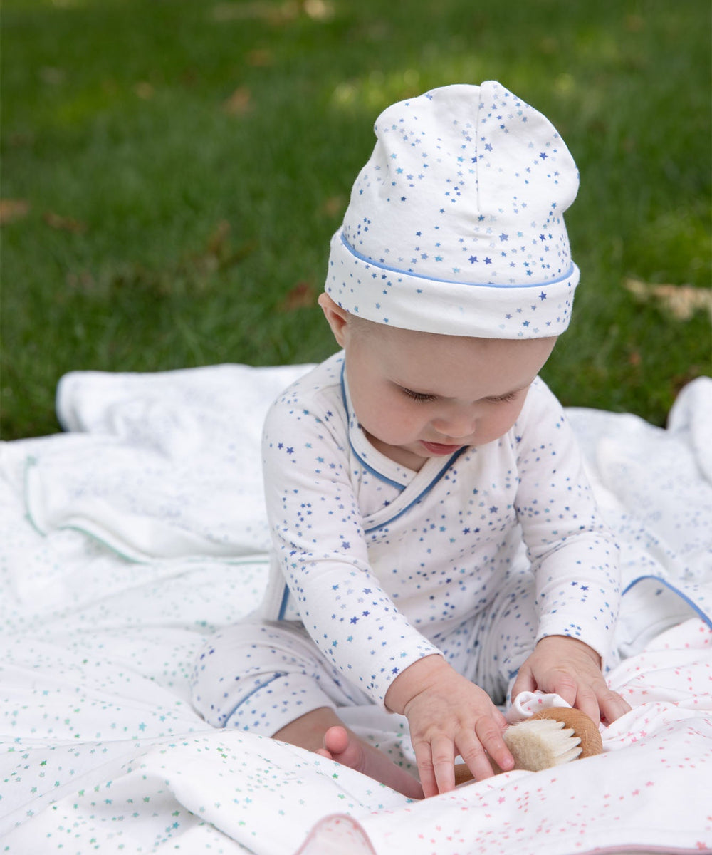 Infant wearing Hazy Hat in Blue Star, sitting on a star-print blanket on grass