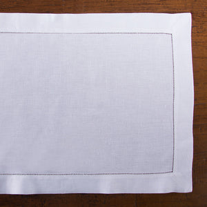 A white linen placemat with a hemstitch border placed on a wooden table.