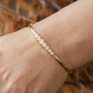 The Graduated Hexagon Bezel Set Diamond Bangle, showcasing alternating hexagon and round diamonds, sparkles on a wrist against a brown patterned fabric background.
