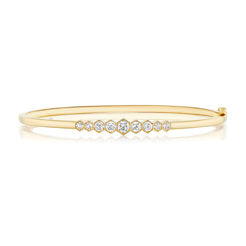 The Graduated Hexagon Bezel Set Diamond Bangle in 18k gold features a row of round white diamonds in graduated sizes set across the top, shown on a white background.