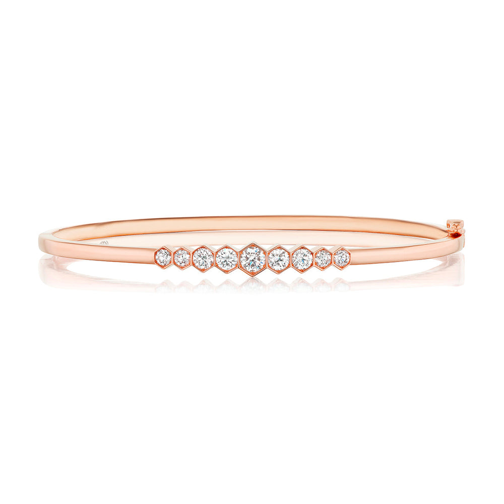 The Graduated Hexagon Bezel Set Diamond Bangle features round white diamonds in graduated sizes, set in 18k rose gold with a sleek, polished finish and minimalist, elegant style.