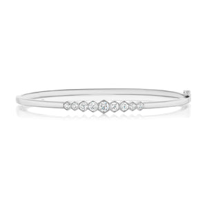 The Graduated Hexagon Bezel Set Diamond Bangle showcases a sleek silver design with round and hexagonal diamonds bezel set in the center, arranged in a graceful graduated pattern.