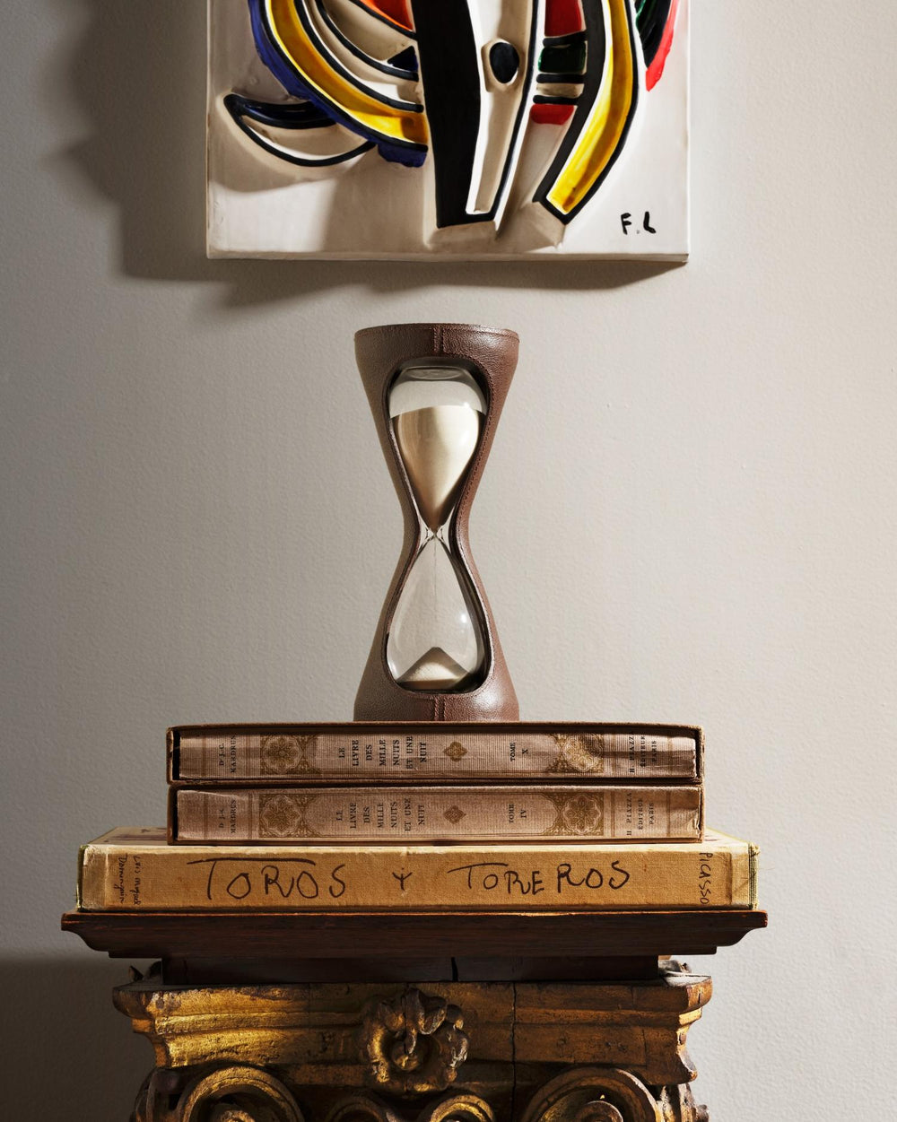 Leather-wrapped hourglass with beige sand sitting on stacked antique books on a carved gilt pedestal