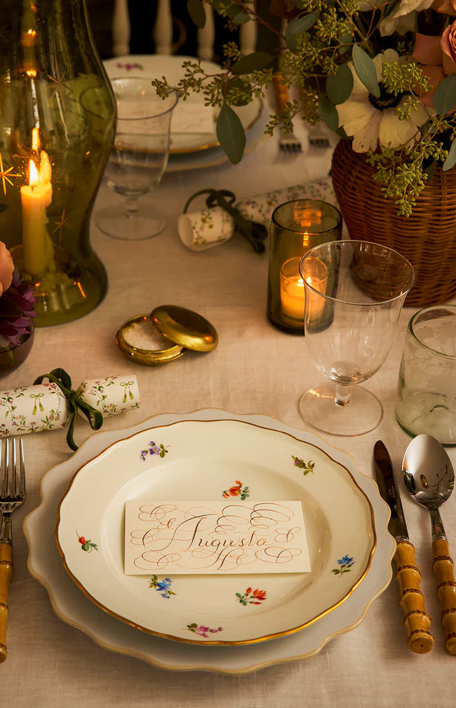 Dark olive star-etched hurricane vase with lit candle casting a patterned glow over table set with floral china and glassware
