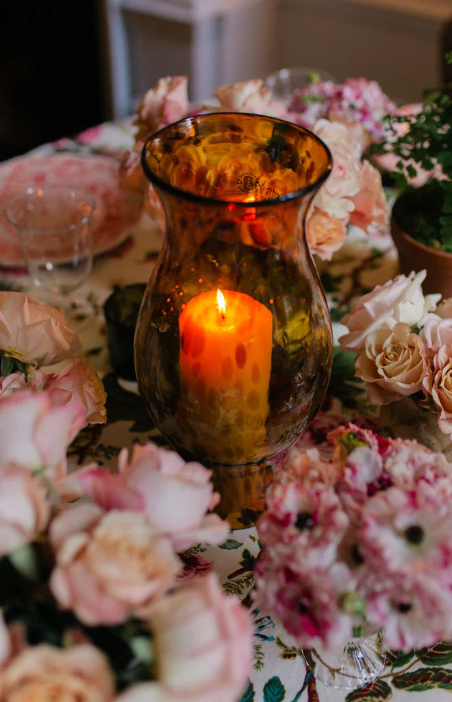 Front view of Hurricane in Tortoiseshell blown-glass vase showcasing mottled amber and espresso tones with a lit candle on a floral table