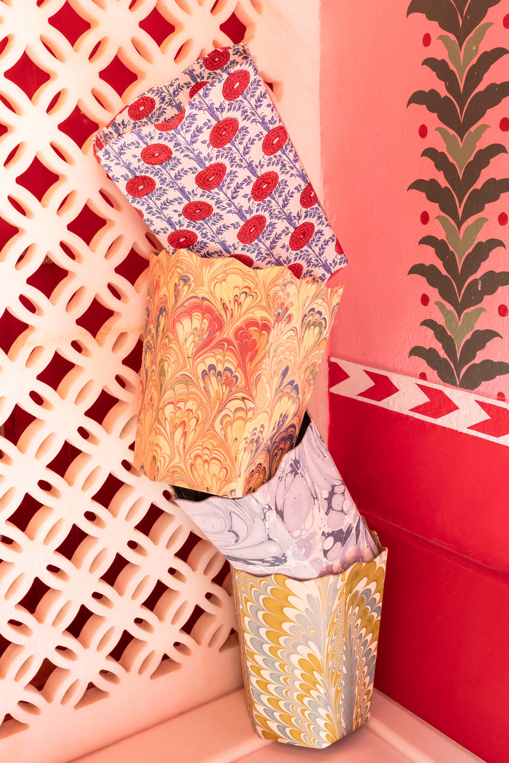 Angled view of three nested Blockprint Scallop waste bins in Araminta showcasing scalloped tops and hand-block-printed floral and marbled patterns against a pink latticed wall