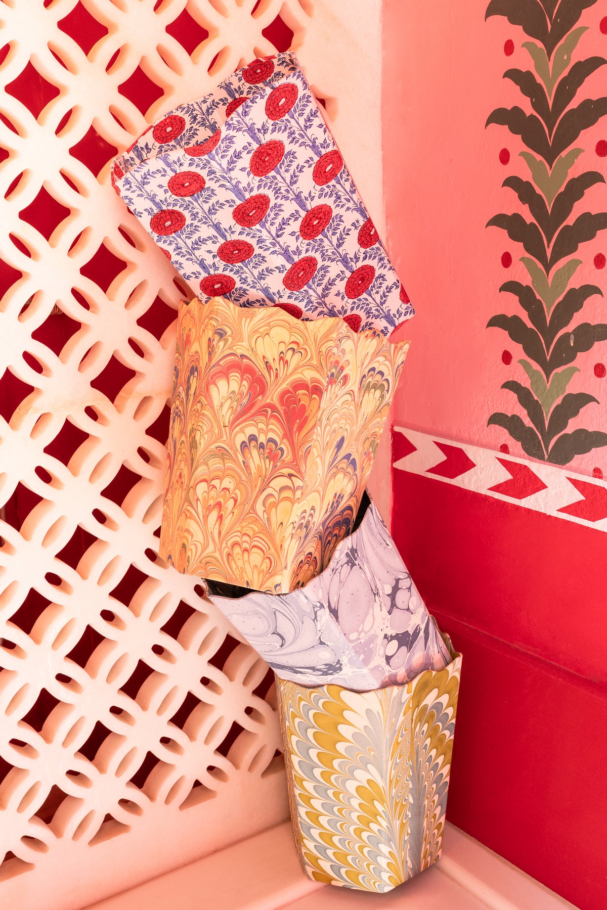 Angled view of three nested Blockprint Scallop waste bins in Araminta showcasing scalloped tops and hand-block-printed floral and marbled patterns against a pink latticed wall