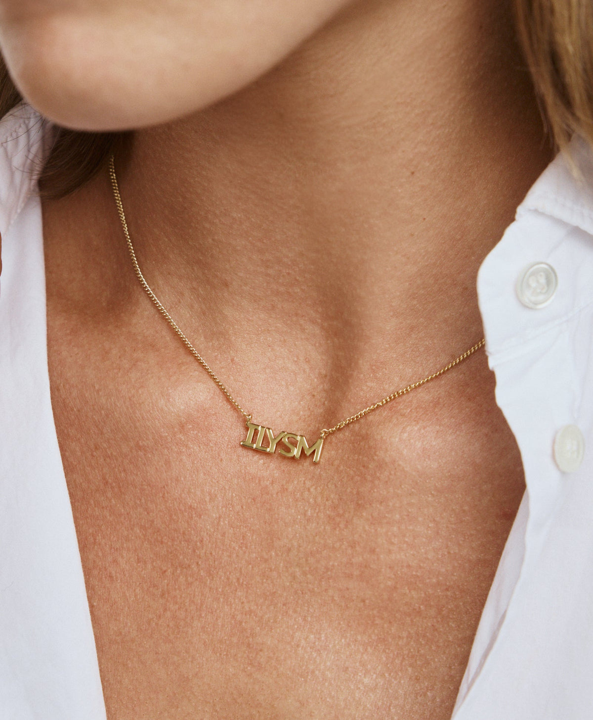 Close-up of The ILYSM Pendant Necklace showcasing its gold tone chain and enamel ILYSM pendant against a white shirt