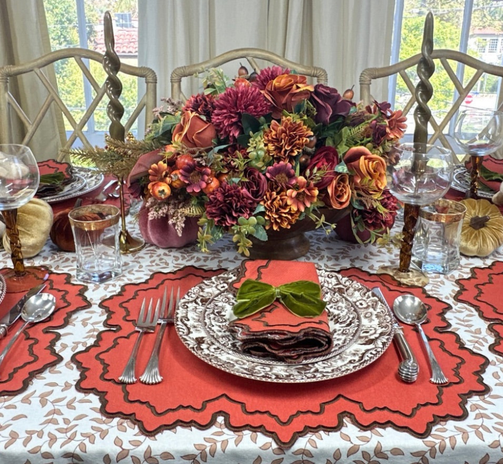 fall table linens Decorative table setting with floral centerpiece, pumpkin placemats, and silverware on a leaves tablecloth.