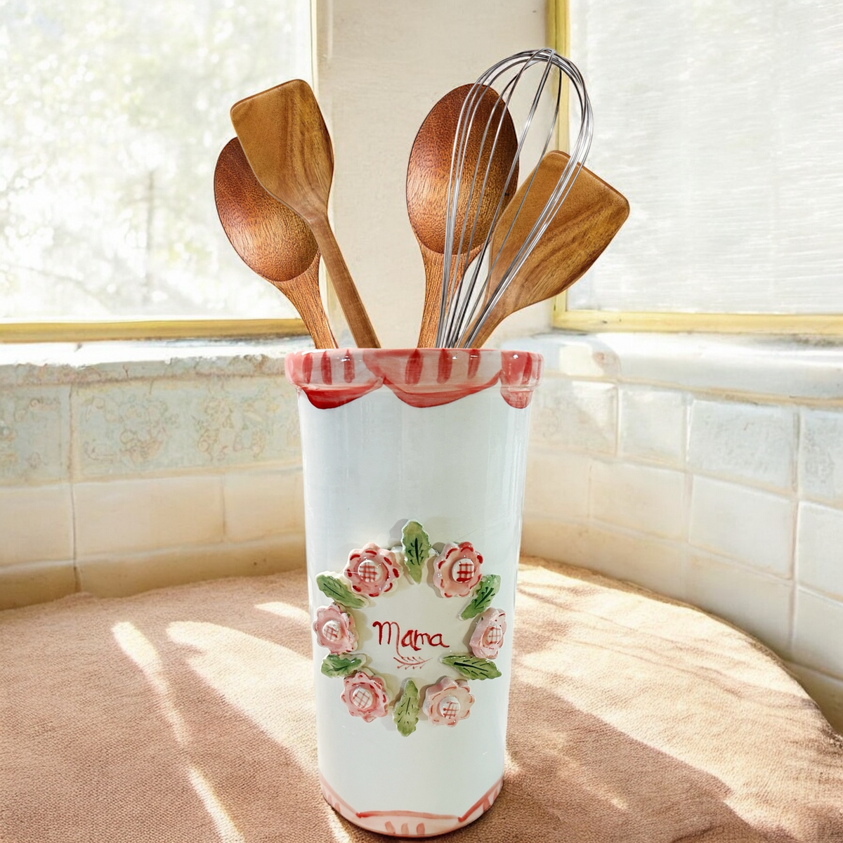 Front of Mama utensil holder with handpainted floral wreath and Mama script, pink rim, with utensils on sunlit windowsill
