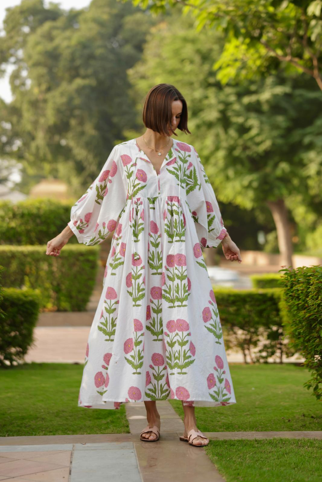 Front view of Taj Maxi Dress in pink flower print showcasing puffed 3/4 sleeves, gathered waist and flowy fit on model in a garden