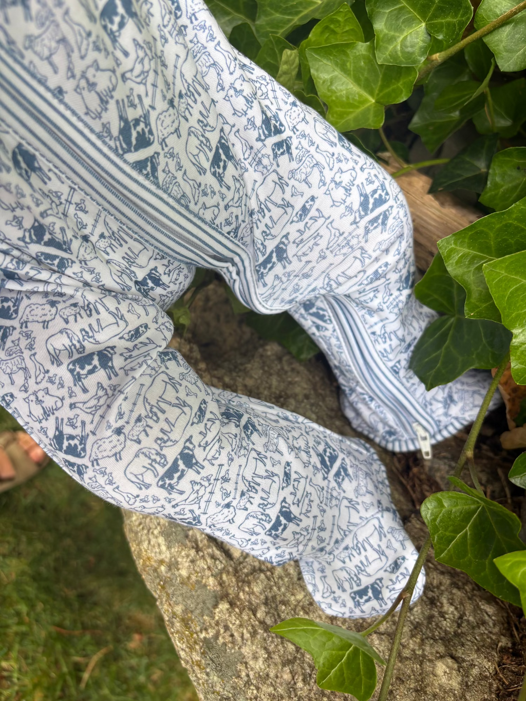 Close-up of Farm Zip Baby Onesie showcasing its blue and white hand-drawn farm animal print on a tree outdoors