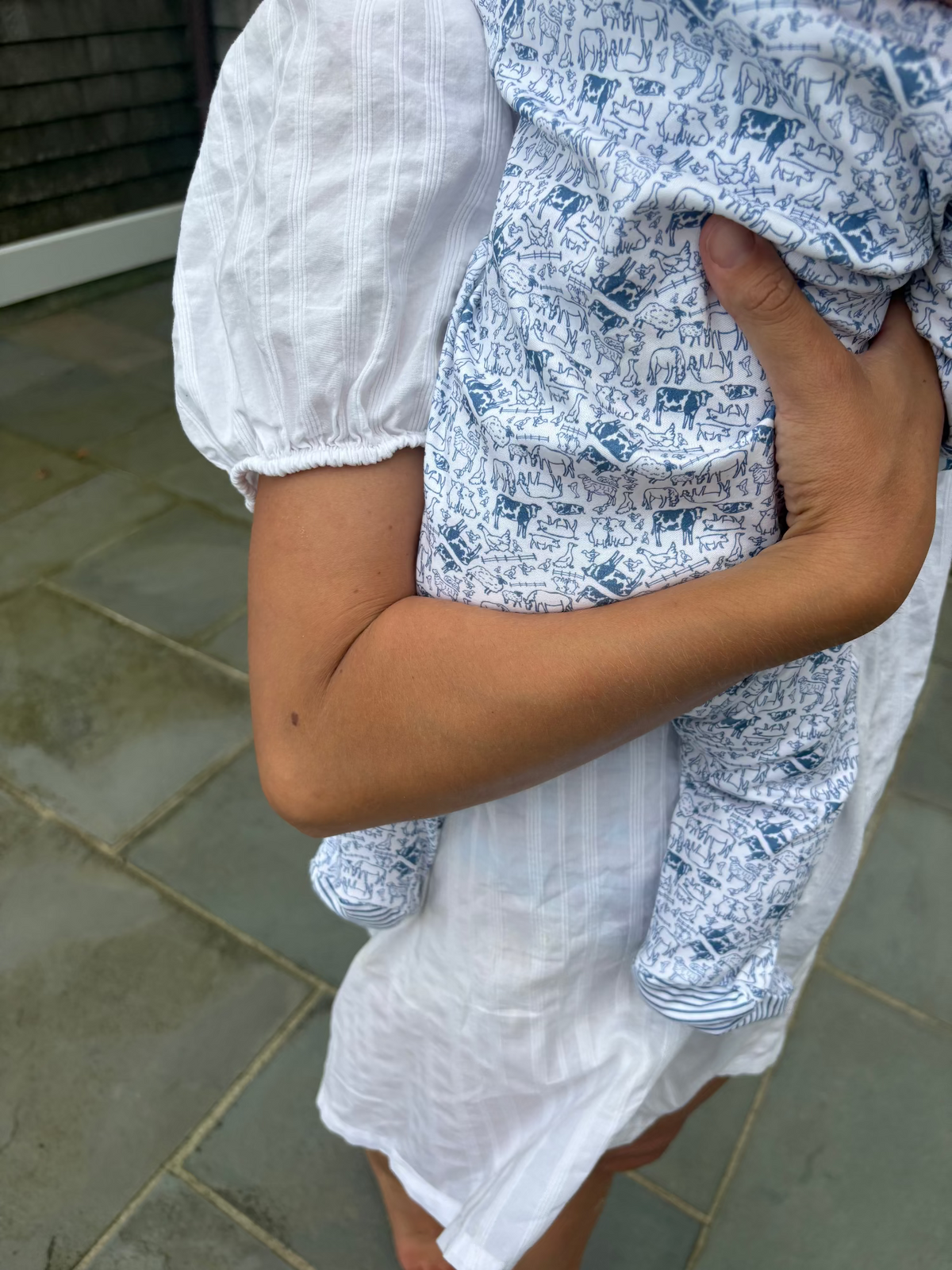 Close-up view of Farm Zip Baby Onesie showcasing a blue and white farm-animal print worn on a baby with a tiled floor background