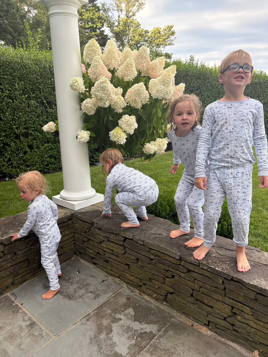 Full view of Farm Kids Henley Pajamas showcasing matching light gray printed long sleeve sets on children with a garden background