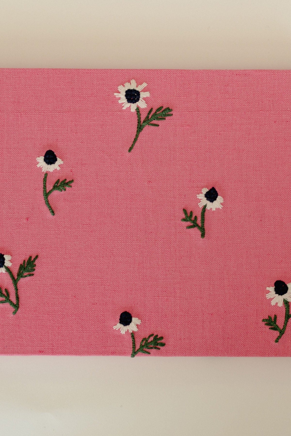 Top view of Manzanilla guest book cover showcasing hand-embroidered white chamomile motifs on pink cotton-linen fabric