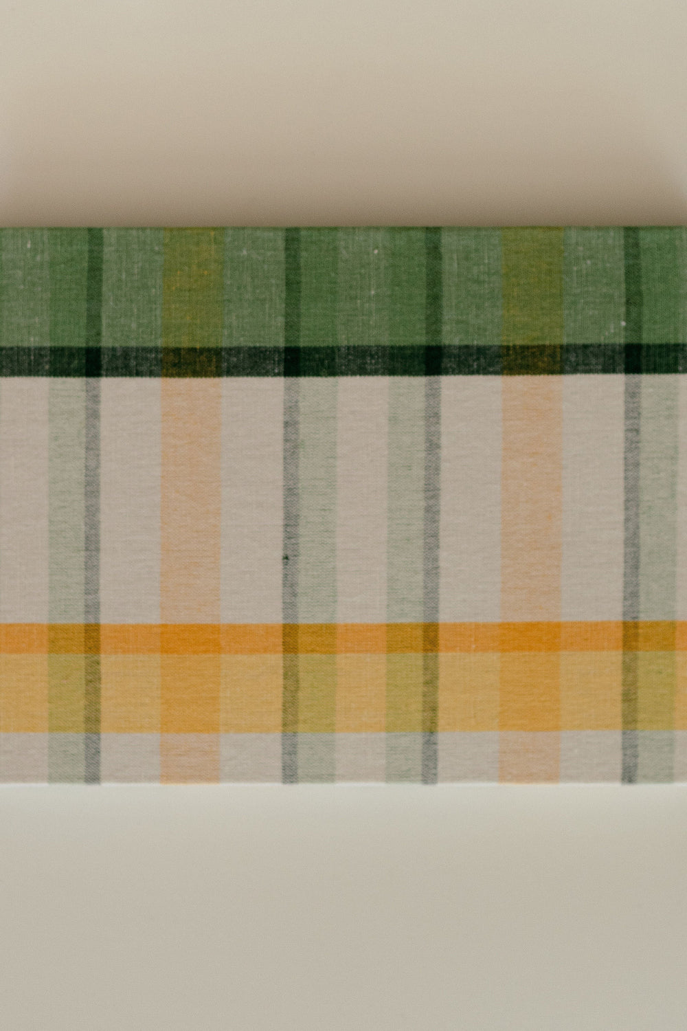 Close-up of guest book cover showcasing green, marigold, and ivory plaid on a cotton-linen texture