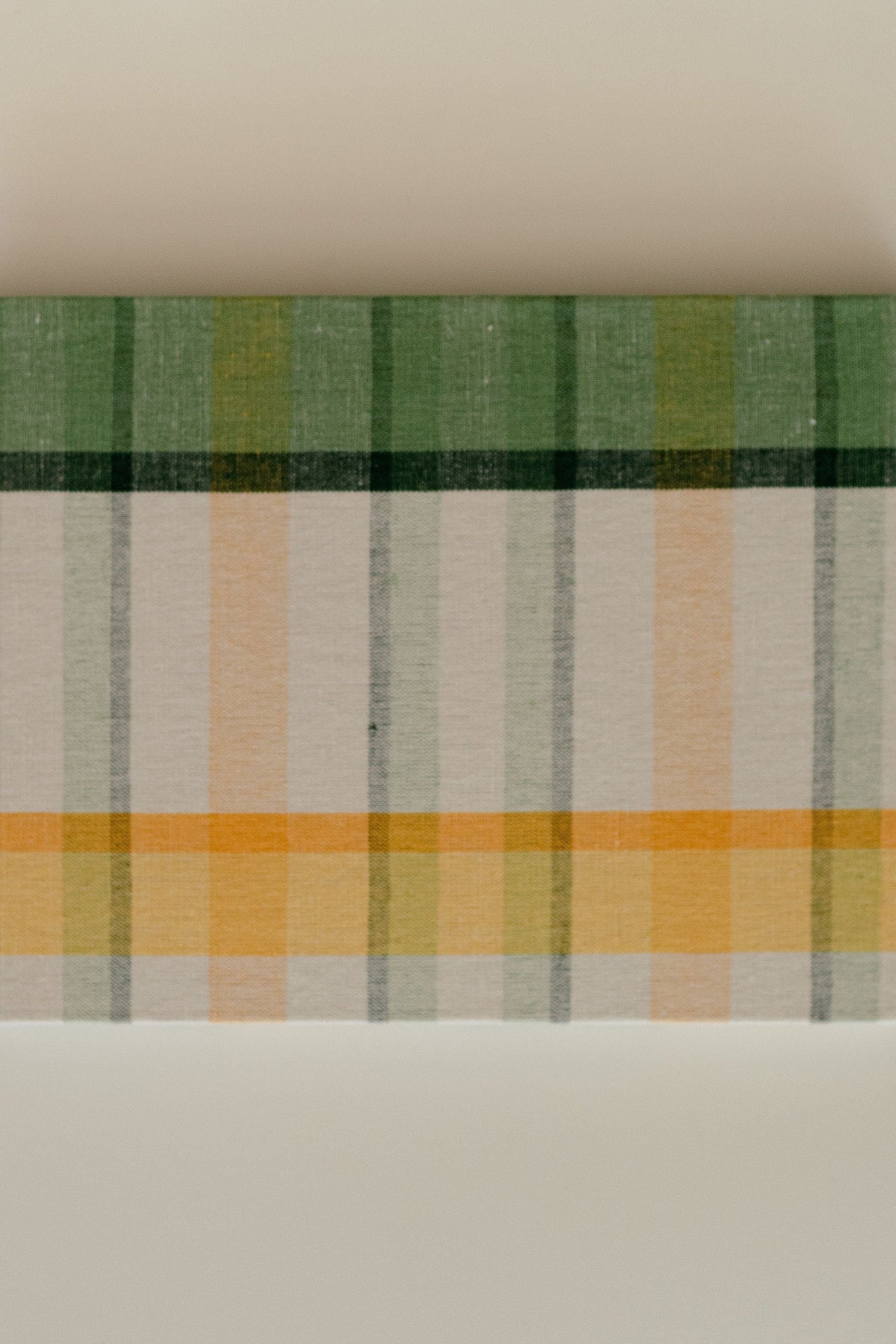 Close-up of guest book cover showcasing green, marigold, and ivory plaid on a cotton-linen texture