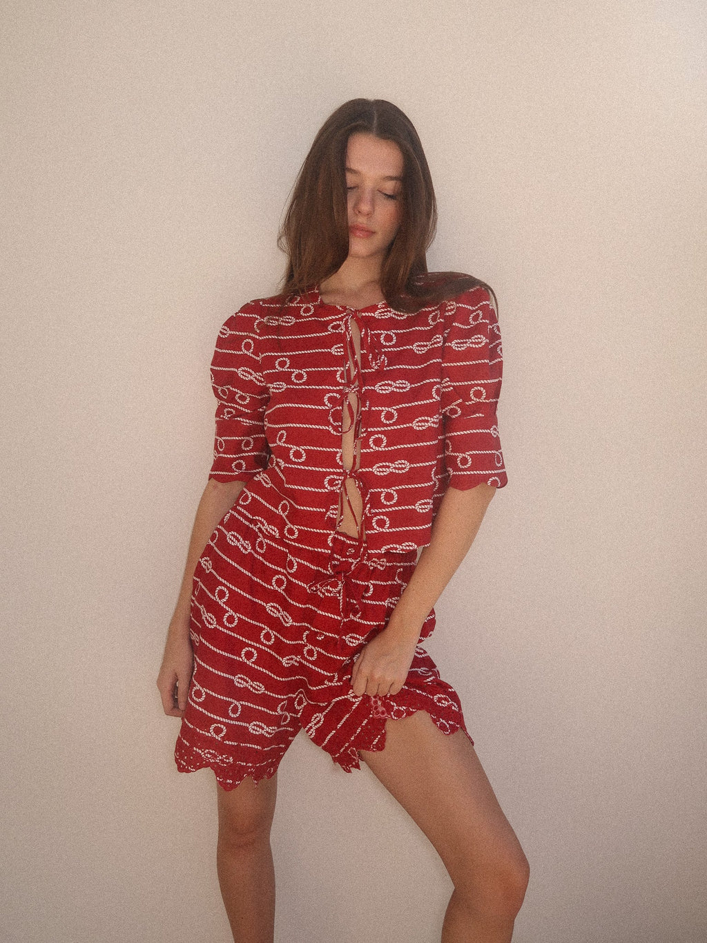 Woman wearing a red dress with white patterns against a plain background
