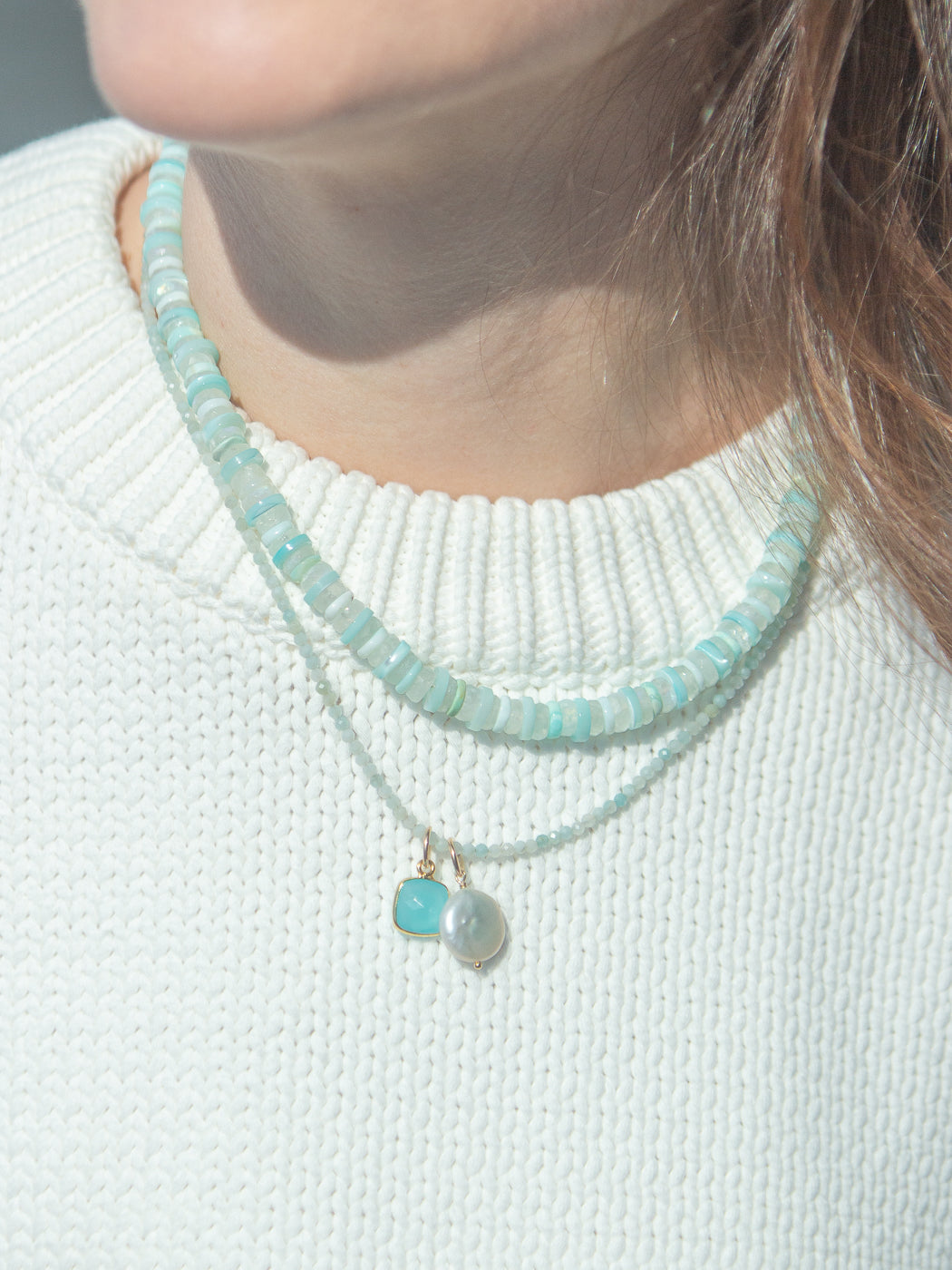 Close-up of Rue Necklace in Light Blue showcasing stacked aqua opal disk beads and a freshwater pearl charm layered on a white knit sweater