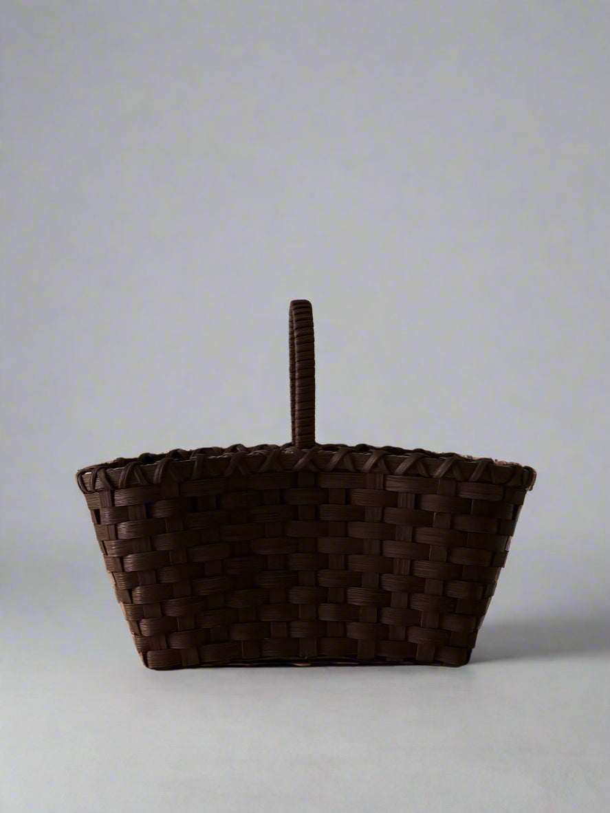 Woven brown basket with a handle on a light gray background