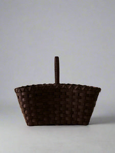 Woven brown basket with a handle on a light gray background