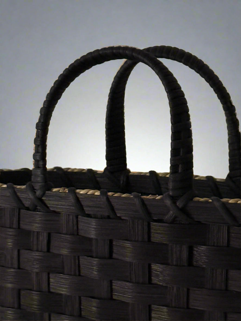 Close-up of a woven basket with black handle on a beige background