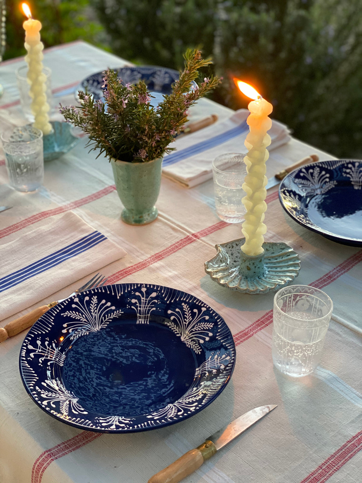Concha seafoam ceramic candle holder with twisted white candle on a striped tablecloth beside blue patterned dinner plates