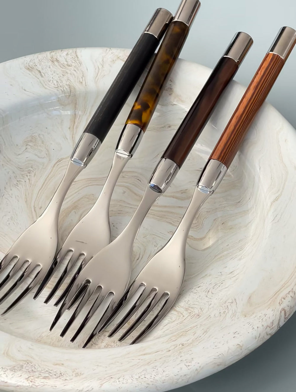 Close-up of Conty place setting forks with chrome-plated bolsters and varied acrylic handles resting in a marbled white bowl