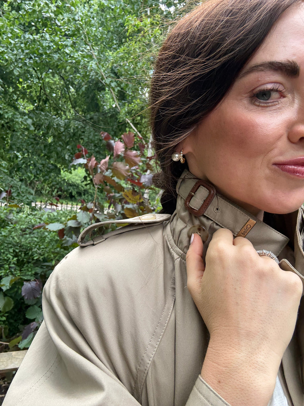 Close-up of The James earrings on model showcasing gold-plated huggie hoops with faux pearl and crystal accents against a leafy outdoor background