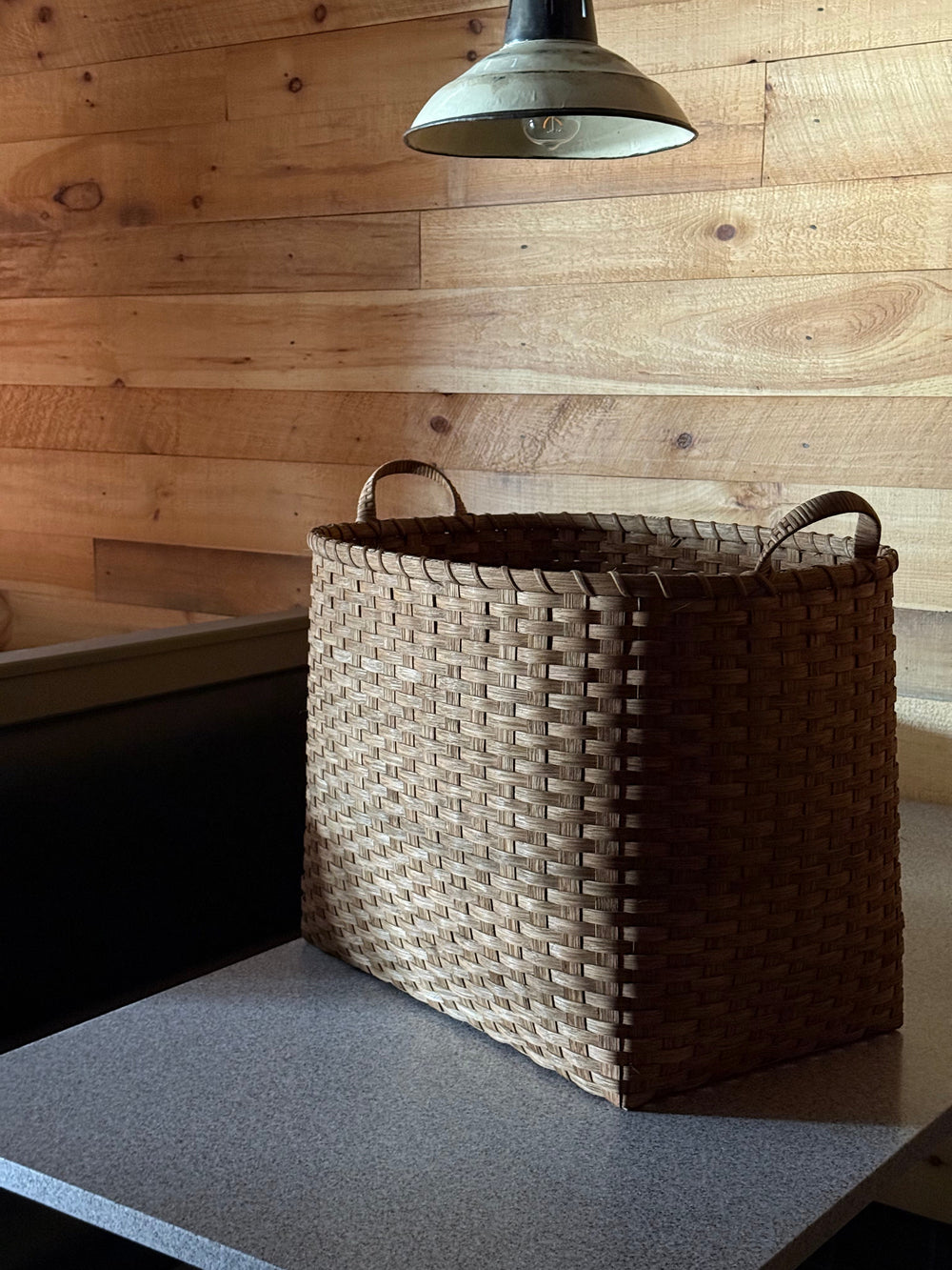 Angled front of Oversized Bounty basket showing woven rattan and wrapped handles against wood-paneled wall