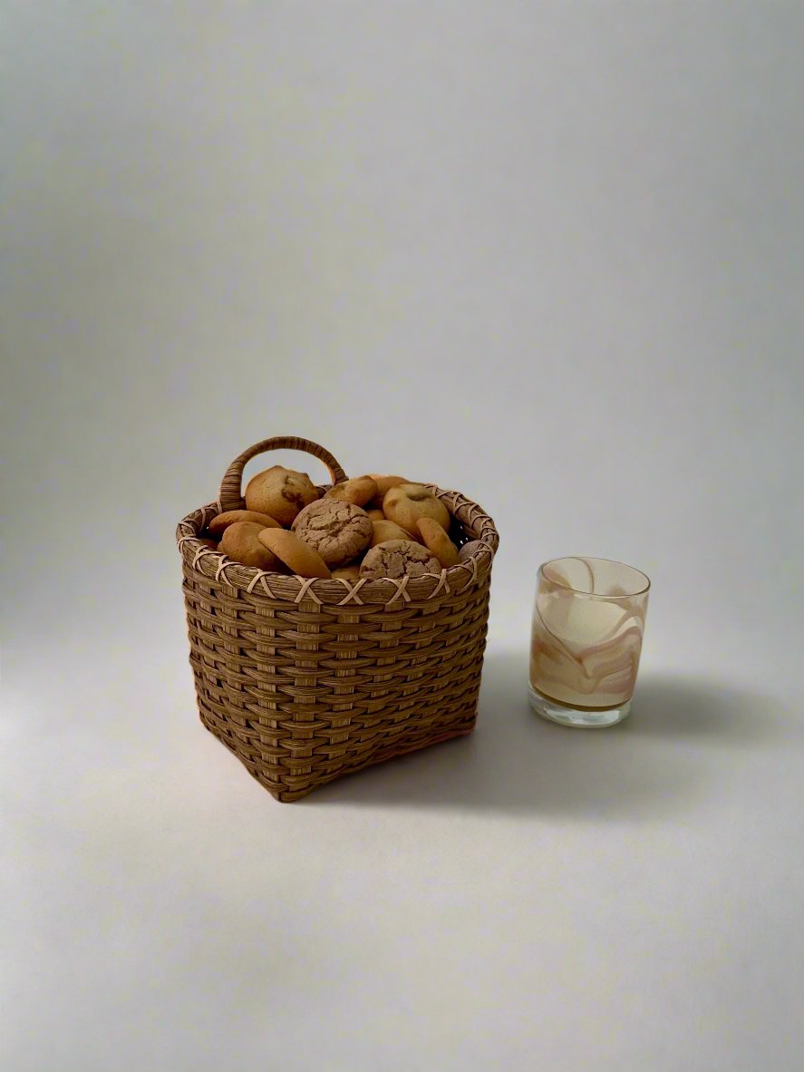 Front view of Panier de Biscuit rattan basket filled with assorted cookies showing woven texture and small glass on neutral background