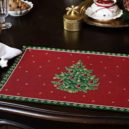 Angled top view of Toys Delight Gobelin placemat showing woven Christmas tree motif and green patterned border on a dark wood table