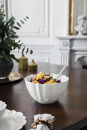 Angled view of Toys Delight Royal Classic large white porcelain bowl showing scalloped rim and embossed motifs on a dark dining table