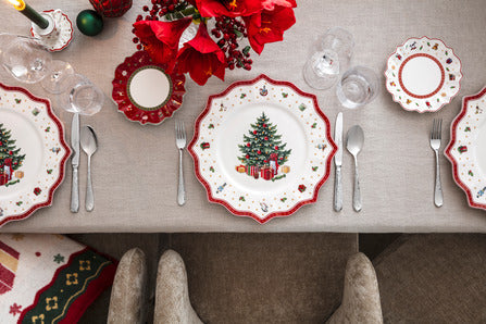 Bread-and-butter plates with scalloped red rims and Christmas tree motif set on a linen table with glassware