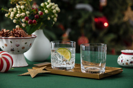 Two short drinking glasses on a gold tray on a green holiday table with Toys Delight footed bowls and Christmas ornaments in the background